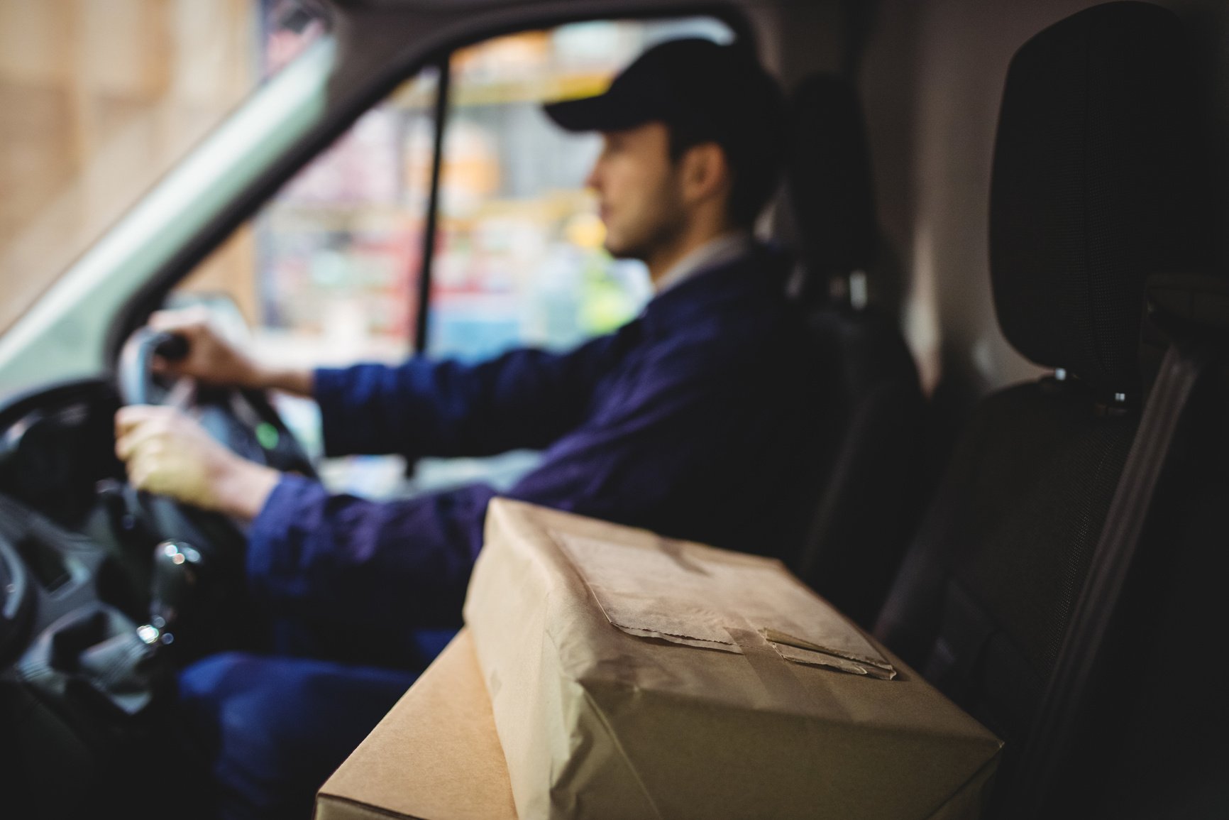 Delivery driver driving van with parcels on seat